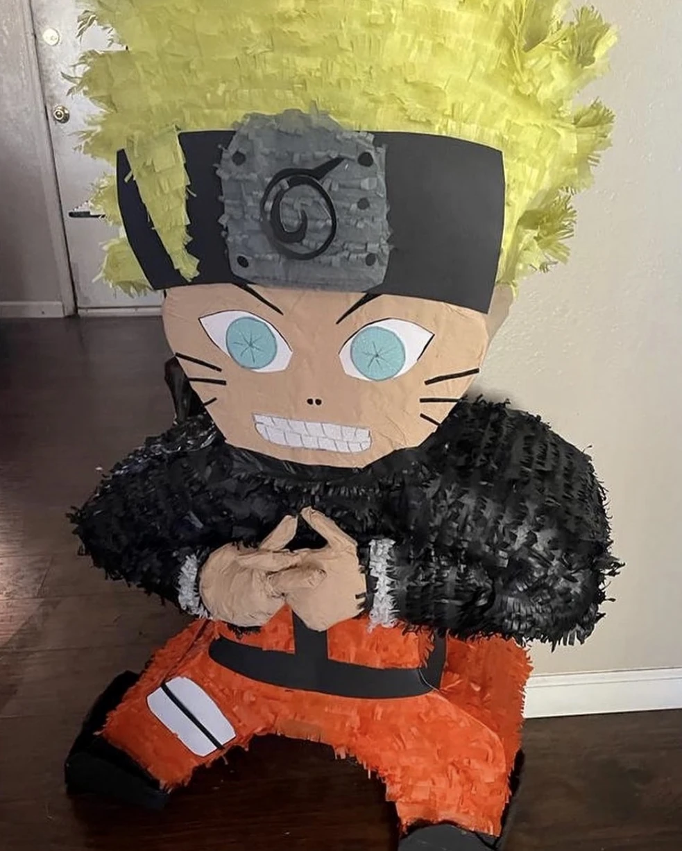 A life-size handmade pi&ntilde;ata of an anime character, standing on a wooden floor, with cut-paper hair and a fringed black collar