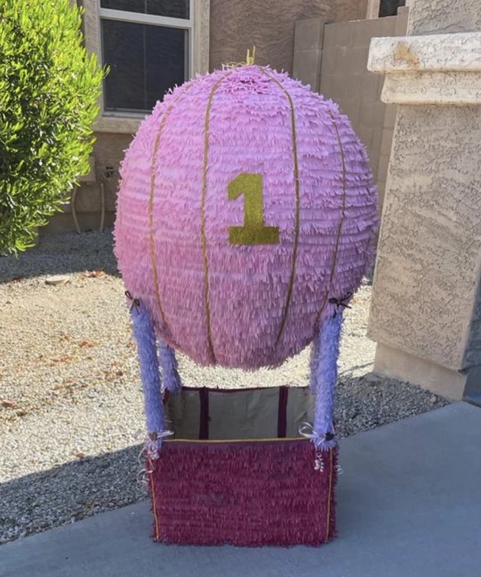 A pastel hot-air-balloon pi&ntilde;ata with a gold number one and a woven basket