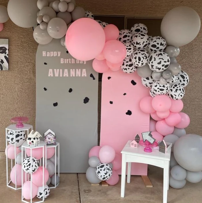 A birthday backdrop in pink, grey and cow print with a balloon garland and a dessert table