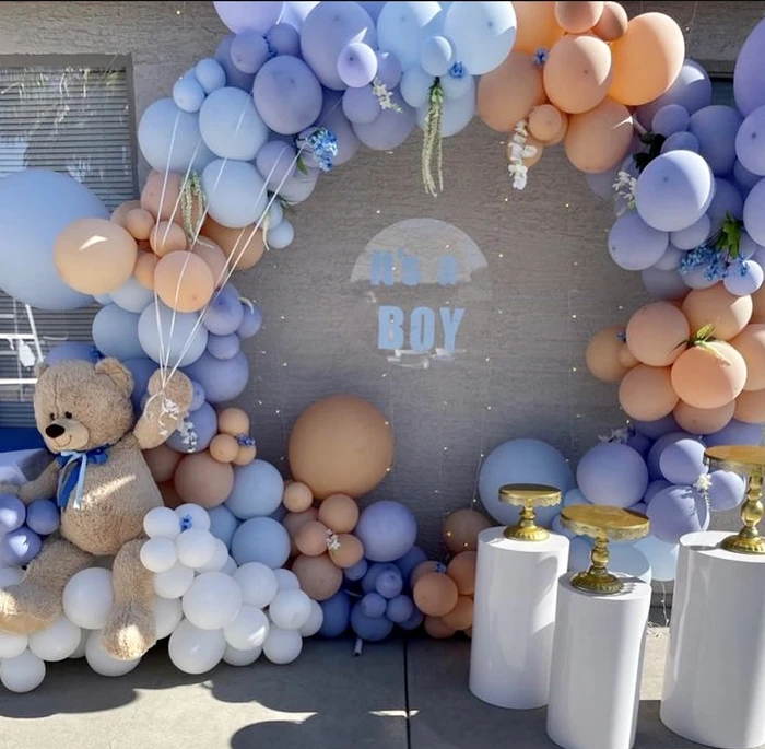 An It's a Boy balloon arch in blue, white and tan with plinths and a teddy bear